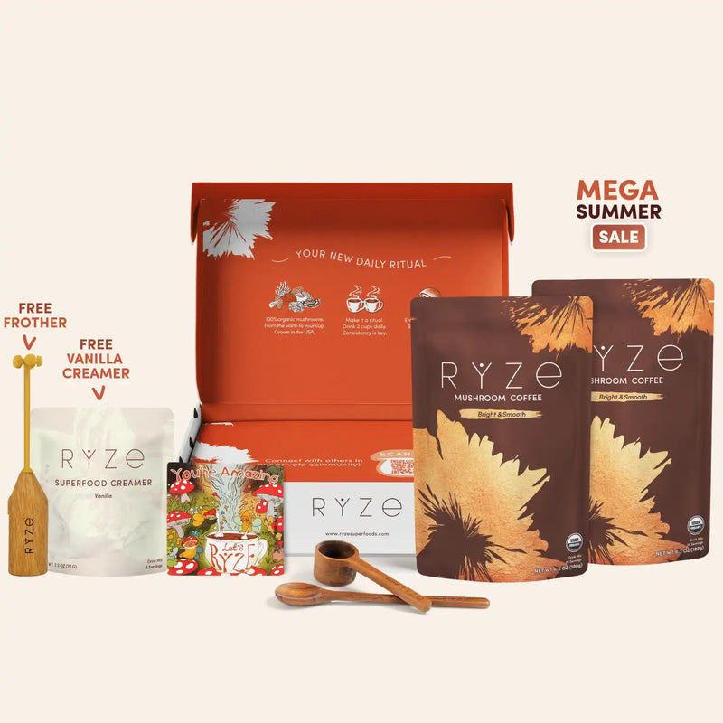 A RYZE coffee gift set arranged on a light beige background, featuring an open orange gift box, two brown and orange RYZE Mushroom Coffee pouches, a white RYZE Superfood Creamer pouch, a small RYZE packet, two wooden measuring spoons, and a wooden funnel. Promotional text reads 'MEGA SUMMER SALE' and 'FREE FROTHER' and 'FREE VANILLA CREAMER'.